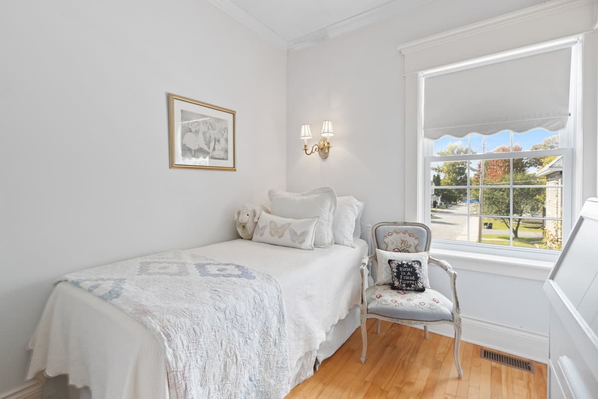 A bright single bedroom with a quilted bed, armchair and garden view